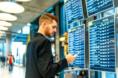 Businessman checking flight information on an airport display while using a smartphone, staying