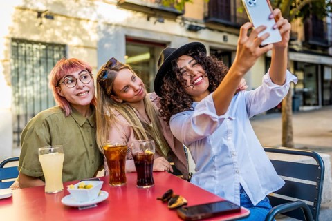 Happy female friends taking selfie sitting on a terrace of a bar