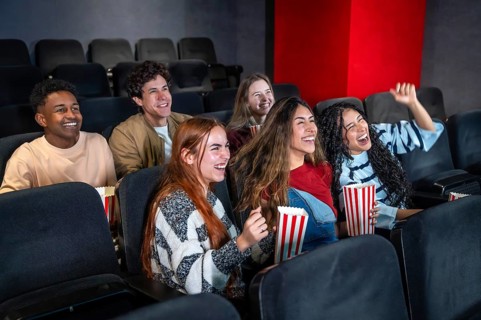 Young people having fun watching a film at the movie theater, eating popcorn and laughing