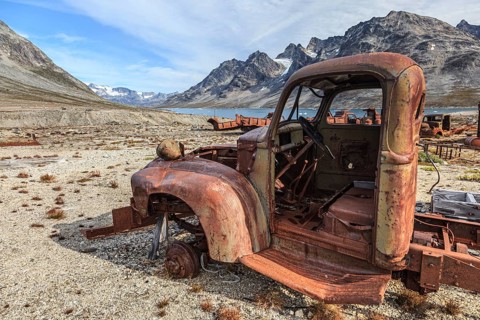 Rusted car and oil drums in front of steep mountains, remains of a US airbase from the Second World