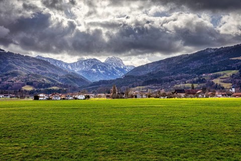 Dramatic Alpine landscape with green meadow in the foreground and cloudy sky over a village, Bad