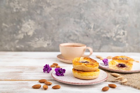 Small cheesecakes with jam and almonds with cup of coffee on a white wooden background and linen