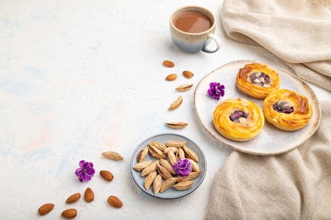Small cheesecakes with jam and almonds with cup of coffee on a white concrete background and linen
