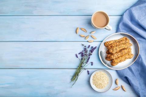 Crumble cookies with seasme and almonds on ceramic plate with cup of coffee and blue linen textile