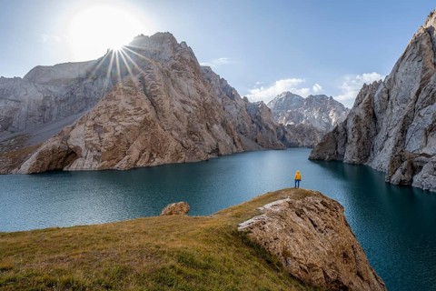 Tourist at the blue mountain lake between rocky steep mountain peaks, Sun Star, Kol Suu Lake, Sary
