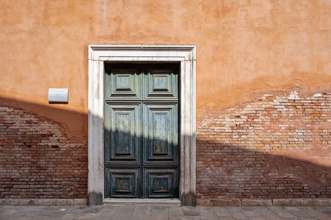 Red house facade with large green door, peeling plaster on brick wall, Venice, Veneto, Italy,