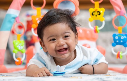 Baby boy playing and smiles lying on bed with pacifier on mouth