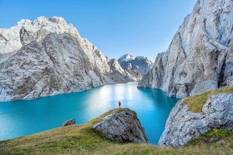 Young man at the turquoise mountain lake Kol Suu with rocky steep mountains, Kol Suu Lake, Sary