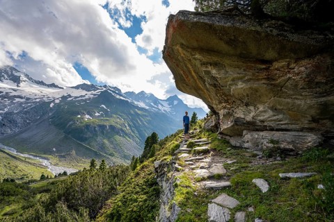 Mountaineer barefoot on a hiking trail under a rocky outcrop, mountain landscape with Waxeggkees,
