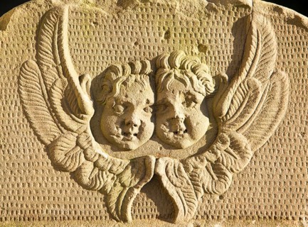 Two angel faces and wings on stone gravestone in church graveyard, Suffolk, England, UK