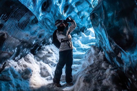 A woman is standing in a cave with snow on the ground. She is wearing a backpack and a white jacket