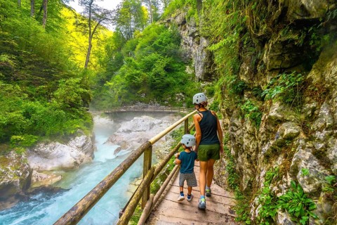 Mother and son wearing helmets walking on wooden path and enjoying breathtaking view of radovna