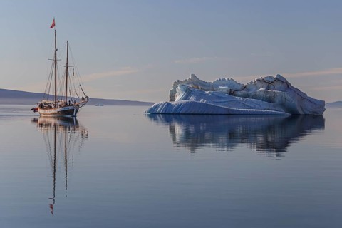 Traditional sailing ship reflected in fjord next to iceberg, sunny, Ittoqqortoormiit, Scoresby
