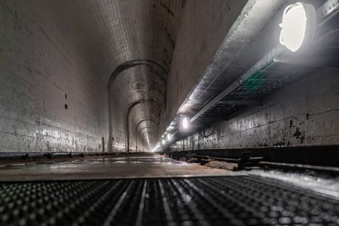 Concrete tunnel with long perspective to the inside, illuminated by lamps at the sides, humid