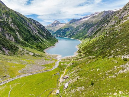 A mountain lake embedded in an alpine landscape with green meadows, mountains, a river and a hiking