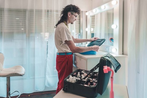Professional makeup artist unpacking cosmetics bag in brightly lit dressing room, preparing for