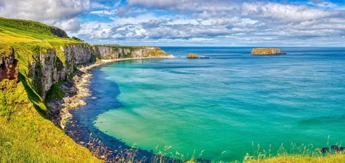 Vast coastal landscape with cliffs and bright blue sea under partly cloudy skies, County Antrim