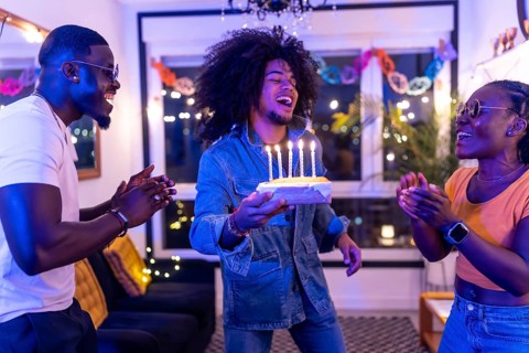 Multi-ethnic friends celebrating birthday party with cake at home at night