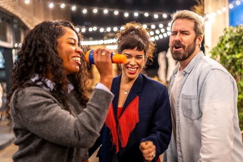 Latin woman singing karaoke next to friends at night party in the terrace of a bar