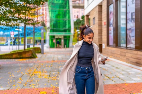 Happy young african american businesswoman using phone while walking on a rush along a city street