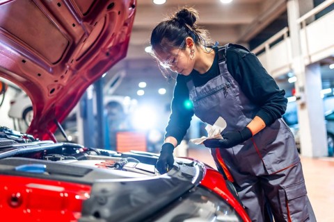 Young woman mechanic inspecting the engine oil level of a red car while working diligently in an