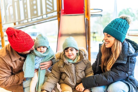 Smiling family with two children wearing winter clothes, hats and scarves enjoying time together on