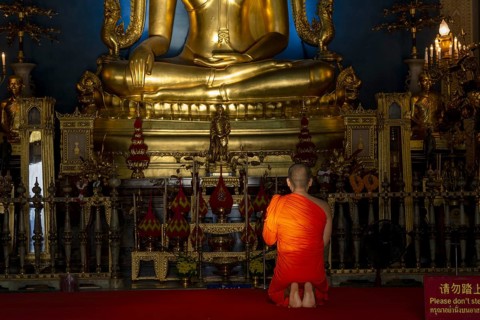 Monk meditating in front of the Phra Buddha Chinnarat, Buddha statue with Bhumispara-mudra, Buddha