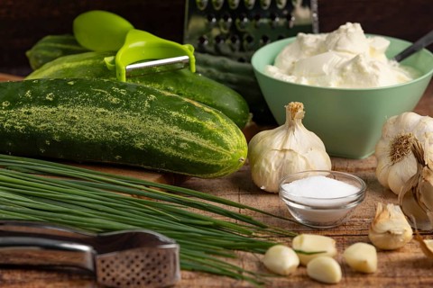 Fresh ingredients such as cucumbers, garlic, chives and sour cream on a wooden table with kitchen