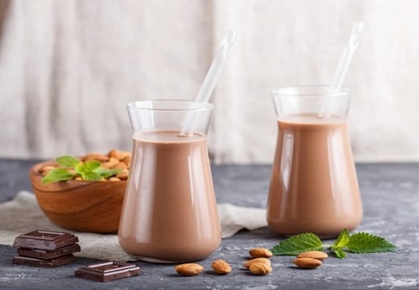 Organic non dairy almond chocolate milk in glass and wooden plate with almond nuts on a black