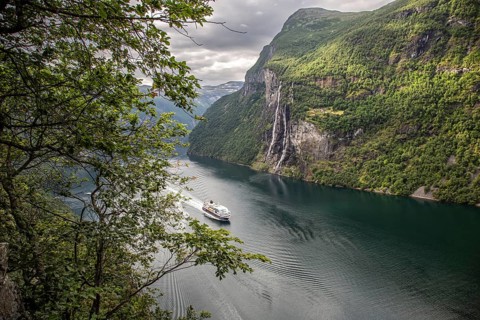 A cruise ship sails through the Gairanger Fjord surrounded by steep mountains and the Seven Sisters