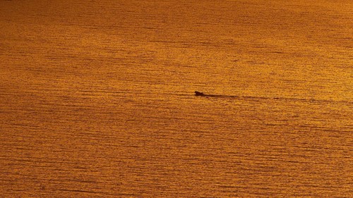 Small boat sails through the calm orange sea at sunset, Kritinia Castle, St John's Castle,