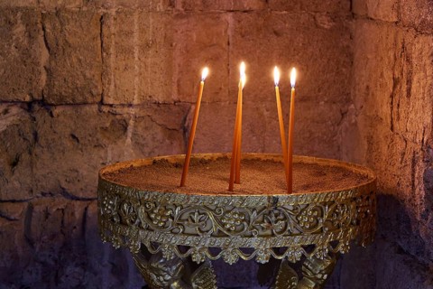 Several burning candles in an antique golden candlestick in front of a stone wall, creating a calm