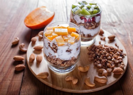 Dessert with greek yogurt, granola, almond, cashew, kiwi and persimmon on brown wooden background.