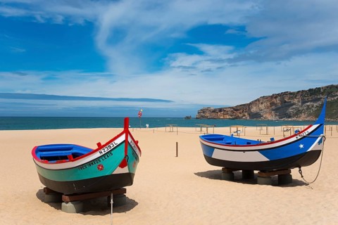 Two fishing boats on the sandy beach of Nazaré with a view of the sea and the cliffs, Praia da