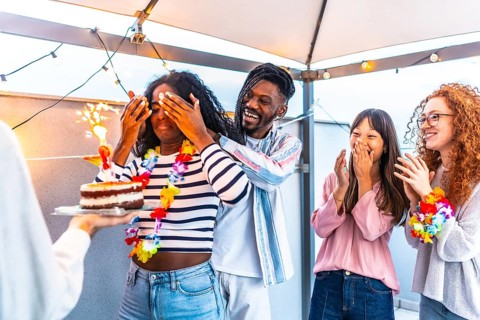 African young woman with eyes covered receiving a birthday cake from multi-ethnic friends at