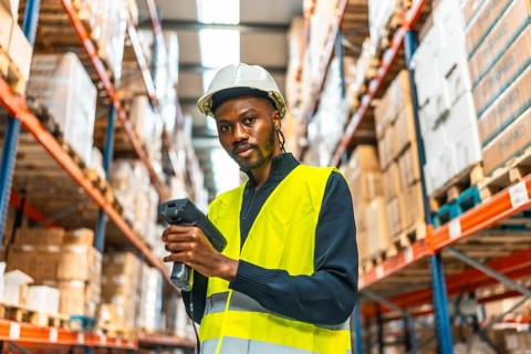 Portrait of an african male worker looking at camera while scanning packages in a warehouse
