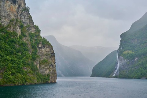 Geiranger Fjord with waterfall surrounded by rocks and mountains with overcast sky, Geiranger,