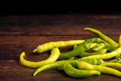 Several green peppers spread on a dark wooden surface, food photography