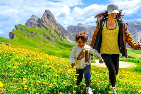 Tourists enjoying summer vacations in the italian alps, running through a field of wildflowers with