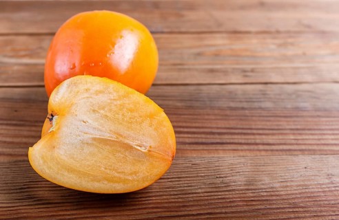 Ripe orange persimmon on brown wooden background, with copy space