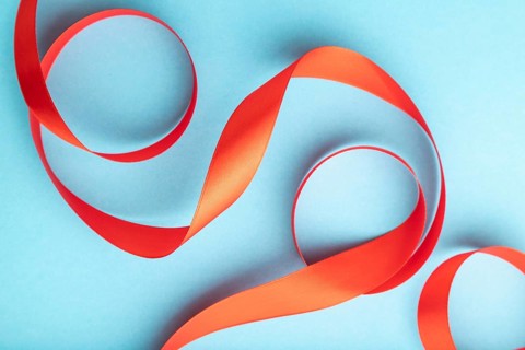 Red coral ribbon on a blue pastel background. Celebration concept. Top view, close up, flat lay