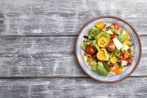 Vegetarian salad of pac choi cabbage, kiwi, tomatoes, kumquat, microgreen sprouts on gray wooden