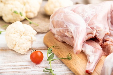 Whole raw rabbit with cauliflower, tomatoes and spices on a white wooden background and linen