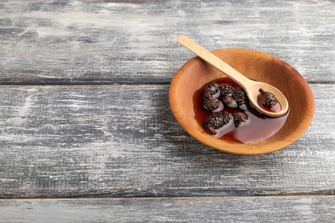 Pine cone jam in wooden bowl on gray wooden background. Side view, copy space