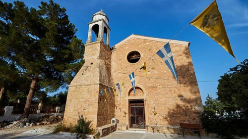 Church entrance with bell tower and Greek flags under a bright blue sky, Koroni, Byzantine