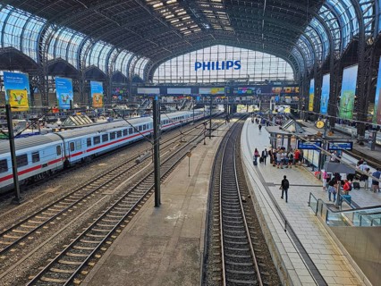 Hamburg central station with several tracks, an ICE train, under a vaulted steel roof, passengers