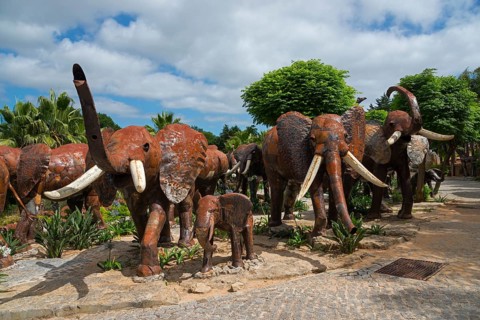 Herd of metal sculptures depicting elephants in a park with trees under a cloudy sky, Bacalhôa,