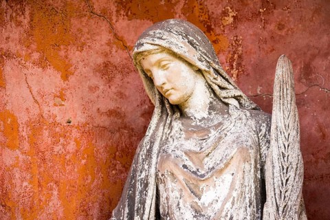 White angel with feather in front of red wall, angel statue, angel figure with peaceful face,