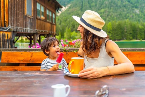 Mother and son enjoying a lakeside snack with a colorful popsicle and warm beverage against a