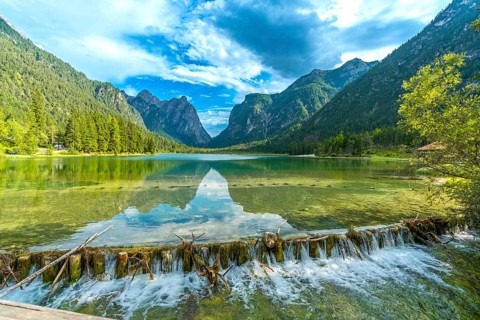 Crystal clear water flowing from lake dobbiaco, surrounded by majestic dolomites peaks, on a sunny